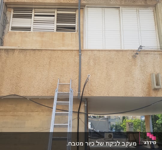 סולם מתכת ליד צינור ביוב חיצוני על קיר בניין